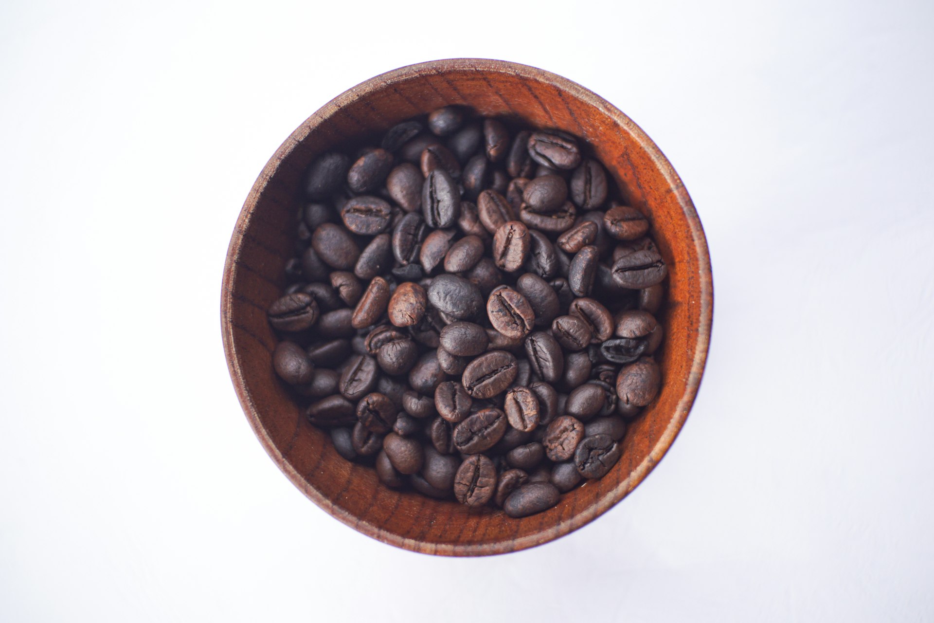Coffee beans sit in a wooden bowl.
